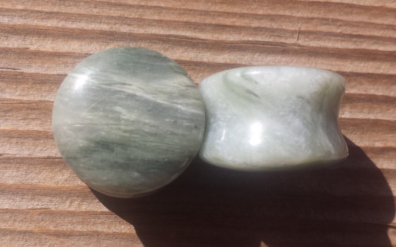 May include: Two green and white marble stone ear gauges. The gauges are round and have a swirling pattern.