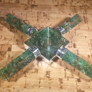 Könnte beinhalten: Eine grüne Kristallpyramide mit vier grünen Kristallspitzen, die von der Basis ausstrahlen. Die Spitzen sind in silbernes Metall gefasst.