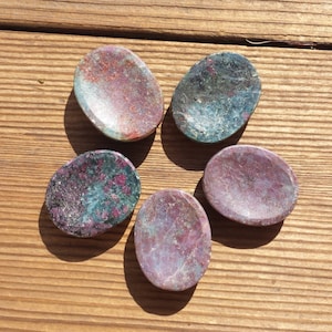 May include: Five oval-shaped polished stones with a variety of pink, green, and black colors. The stones are smooth and have a natural, organic look.
