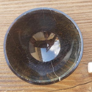 May include: A dark brown, round bowl with a glossy finish. The bowl has a crackled texture and a reflective interior. A white die with the number 8 is next to the bowl.