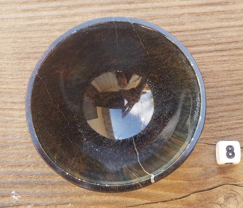 May include: A dark brown, round bowl with a glossy finish. The bowl has a crackled texture and a reflective interior. A white die with the number 8 is next to the bowl.