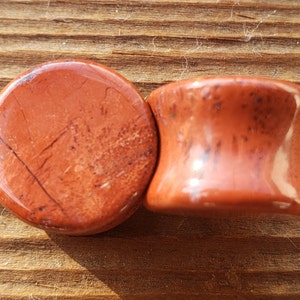 May include: Two red jasper stone ear gauges, one is a flat disc and the other is a flared plug.