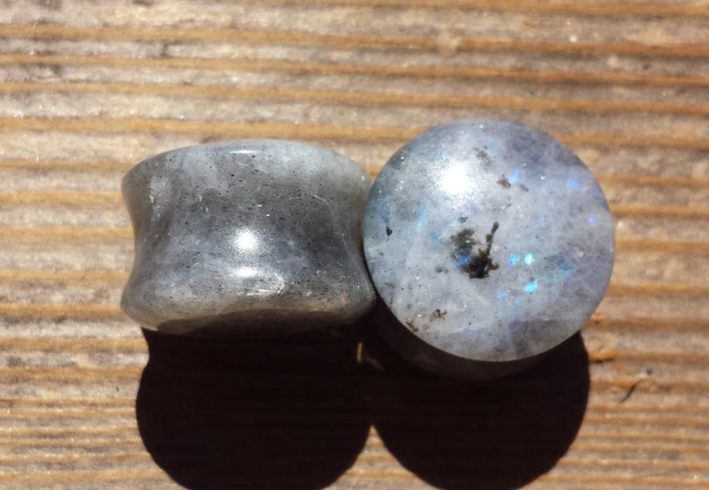 May include: Two round, gray and white gemstone plugs for stretched earlobes. The plugs have a smooth, polished surface and a subtle iridescent sheen.