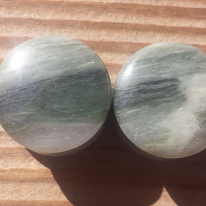 May include: Pair of round green and white stone ear gauges. The gauges have a swirling pattern.