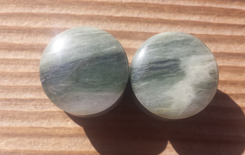 May include: Pair of round green and white stone ear gauges. The gauges have a swirling pattern.