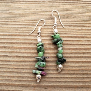 Peut inclure: Une paire de boucles d'oreilles en argent avec des éclats de pierres précieuses vertes et roses. Les boucles d'oreilles sont de style pendantes et ont une fermeture à crochet en argent.