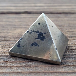 May include: A silver-toned pyramid-shaped crystal with a rough, textured surface.