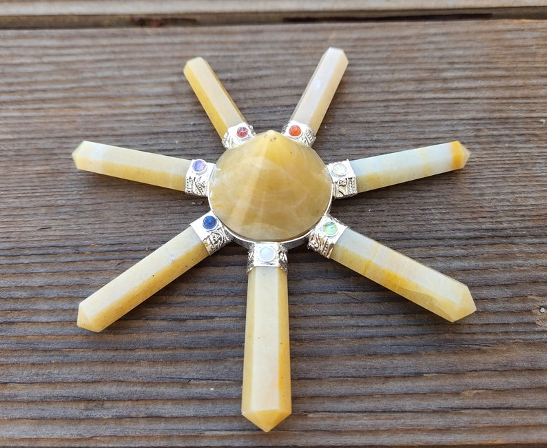May include: A yellow crystal pyramid with seven yellow crystal points radiating outward. The points are arranged in a star shape. Each point has a small, colorful gemstone at the end.