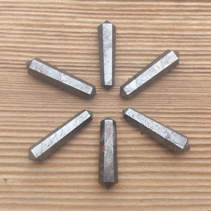 May include: Six silver-colored, pointed, crystal wands arranged in a starburst pattern on a wood surface.