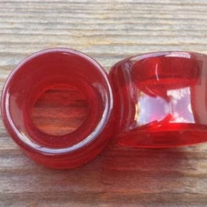 May include: Two red acrylic ear gauges, one is a flared style and the other is a straight style.