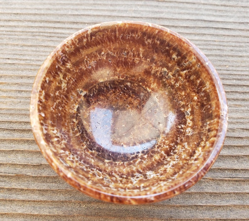 Pu&ograve; includere: Una piccola ciotola rotonda con una superficie lucida e macchiettata. Il colore della ciotola &egrave; un mix di marrone e beige, con una finitura lucida. La ciotola &egrave; probabilmente fatta di pietra o un materiale simile.