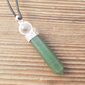 Könnte beinhalten: Ein grüner Kristallspitzen-Anhänger mit einer klaren Kristallkugel oben, der an einer schwarzen Schnur hängt.