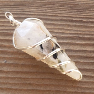 May include: A white crystal point pendant wrapped in silver wire. The crystal has black inclusions and is set in a silver bail.