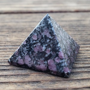May include: A black and pink speckled pyramid-shaped crystal.