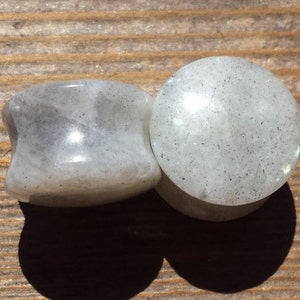 May include: Pair of white stone ear gauges with a speckled texture. The gauges are round and have a smooth, polished finish.