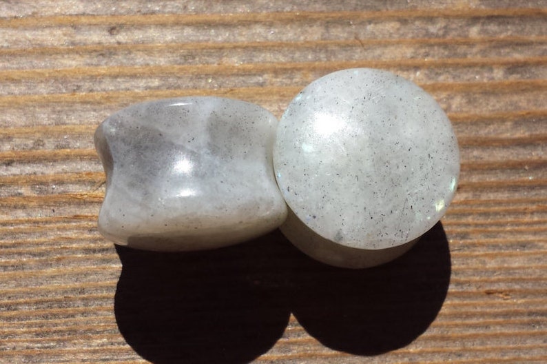 May include: Pair of white stone ear gauges with a speckled texture. The gauges are round and have a smooth, polished finish.