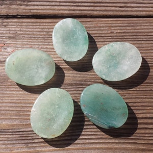 May include: Five smooth, oval-shaped green jade stones. The stones are polished and have a light green color with some darker green veins.