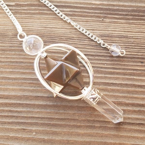May include: A brown crystal pendulum with a clear quartz point and a silver chain. The crystal is shaped like a star and is surrounded by a silver ring.