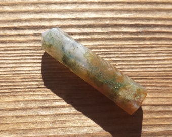 May include: A green, brown and white agate crystal point, also known as a wand, on a wooden surface.