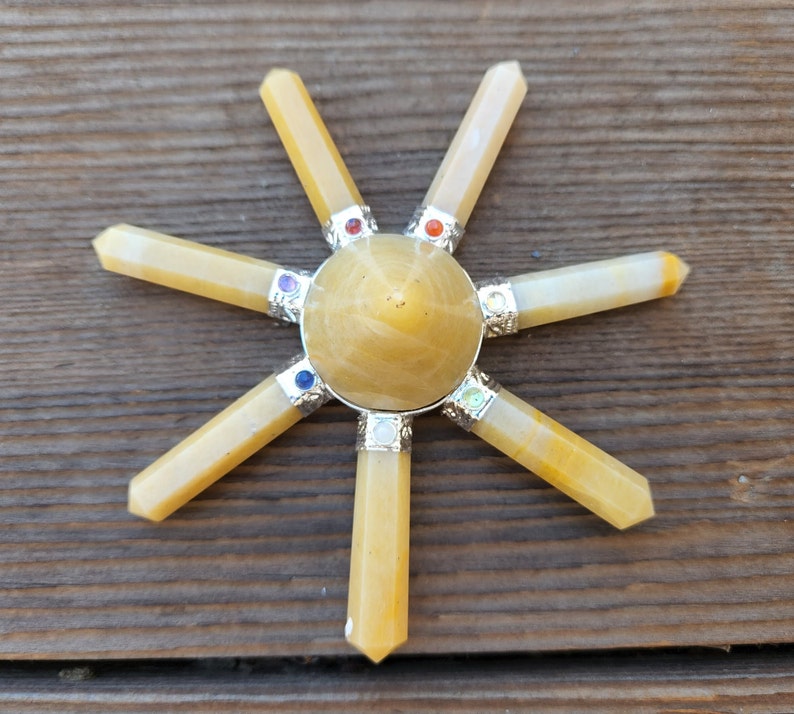 May include: A seven-pointed crystal chakra healing grid made of yellow citrine points with a central citrine pyramid. The points are arranged in a circle around the pyramid, and each point has a small silver bead at its base.