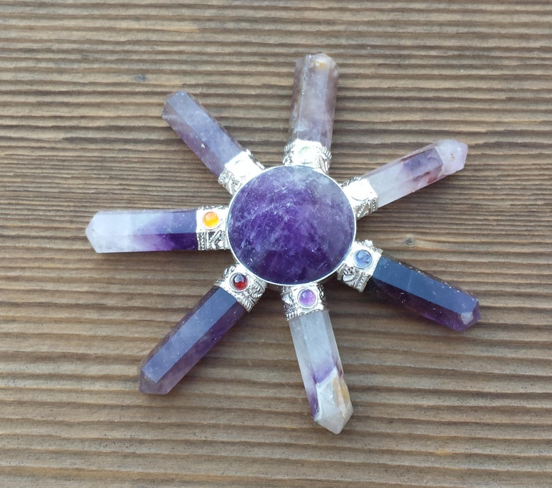 May include: Amethyst crystal chakra balancing wheel with seven chakra stones. The wheel is made of polished amethyst and has a round shape. The chakra stones are arranged in a circle around the wheel and are each a different color.