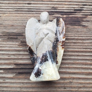 May include: A carved angel figurine made of brown and white banded agate. The angel has a long flowing robe and wings.