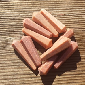 May include: A group of eight pink and white gemstone points, also known as wands, are arranged on a wooden surface. The points are all roughly the same size and shape, and they have a smooth, polished finish.