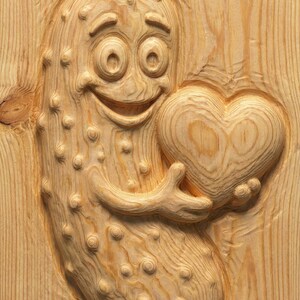 May include: A wooden carving of a smiling pickle character holding a heart. The pickle has a friendly expression and is covered in small bumps. The heart is also carved from wood, with visible grain.