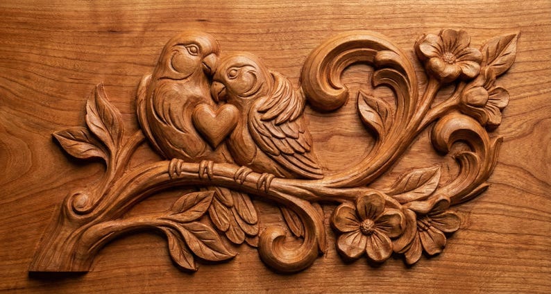 May include: A detailed wood carving of two birds nestled together, with a heart shape between them. The birds are perched on a branch with leaves and flowers. The carving is made of a warm, light brown wood.