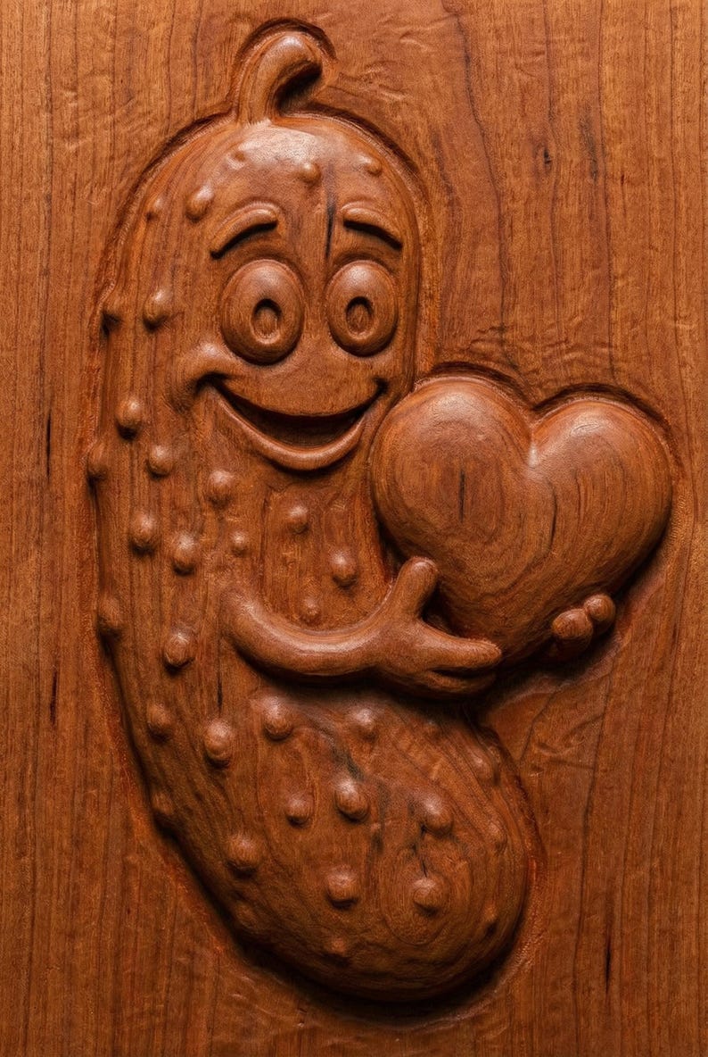 May include: A wooden carving of a smiling pickle character holding a heart. The pickle has a happy expression and is covered in small bumps. The heart is smooth and detailed, and the carving is set against a wood grain background.