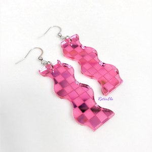 May include: A pair of pink, wavy earrings with a checkered design. The earrings have a shiny, reflective surface and are attached to silver-coloured ear wires. The word "RetroElo" is printed on the right earring.