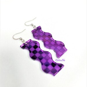 May include: A pair of purple, wavy-shaped earrings with a checkered pattern. The earrings are made of a reflective material and have silver-coloured hooks. A unique accessory.