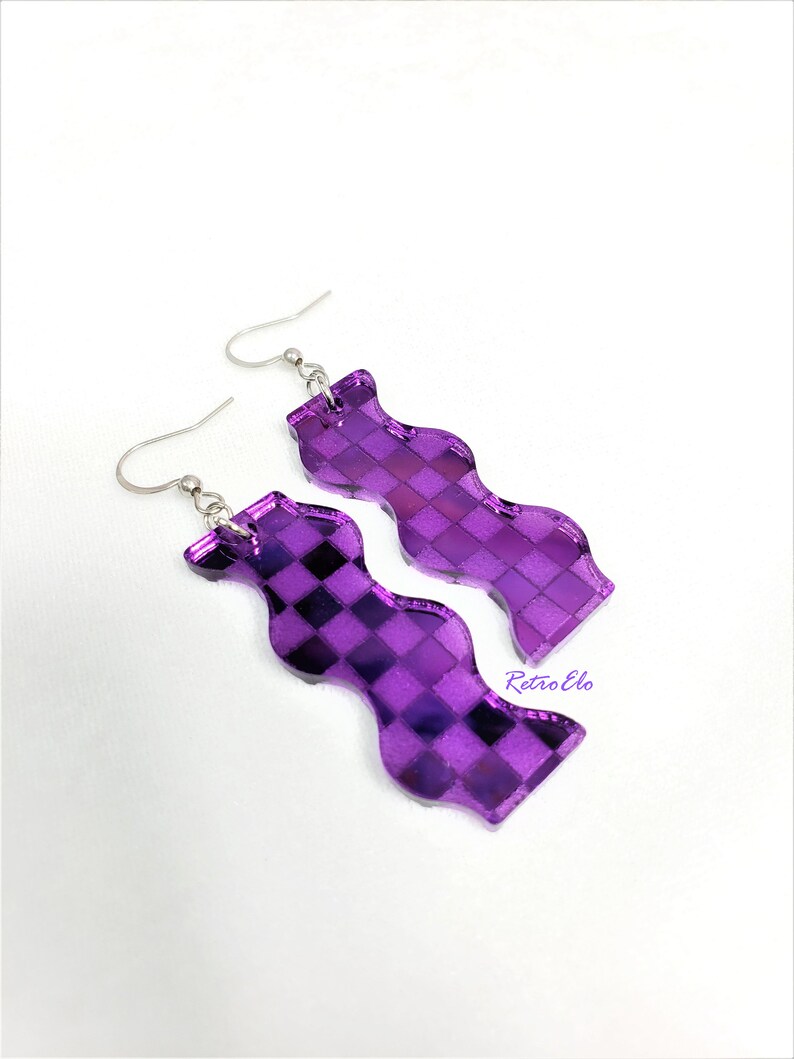 May include: A pair of purple, wavy-shaped earrings with a checkered pattern. The earrings are made of a reflective material and have silver-coloured hooks. A unique accessory.