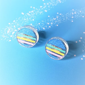 May include: A pair of round, blue and white earrings with glitter and colorful stripes.