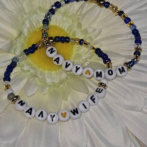 May include: Two beaded bracelets with gold and blue beads spelling out "Navy Mom" and "Navy Wife" with a gold heart charm on each.