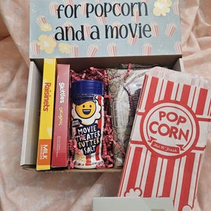 May include: A gift box filled with movie night snacks, including popcorn, Skittles, Raisinets, milk chocolate, and movie theater butter salt. The box also includes a gift card.