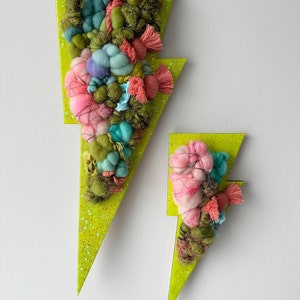 May include: Two decorative wall hangings in the shape of lightning bolts. The bolts are lime green with glitter and feature textured yarn in shades of pink, blue, and green. The larger bolt is approximately 24 inches tall.