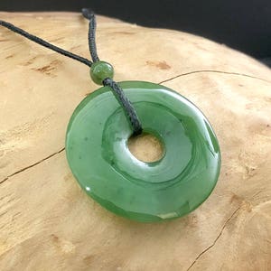 May include: A green jade pendant in the shape of a ring, hanging from a black cord. The pendant is smooth and polished, with a hole in the center.