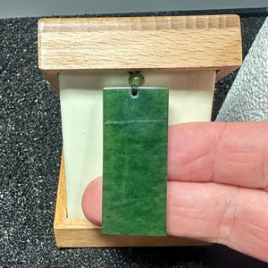 May include: A green jade pendant with a black cord, displayed in a wooden box.