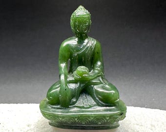 May include: A small green jade Buddha statue sitting in a meditative pose with a lotus flower in its hands. The statue is carved with intricate details and has a serene expression.