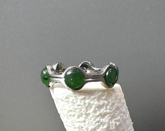May include: A silver ring with four green gemstones set in a circular design.