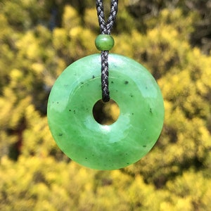 May include: A green jade pendant in the shape of a donut, hanging from a black cord.