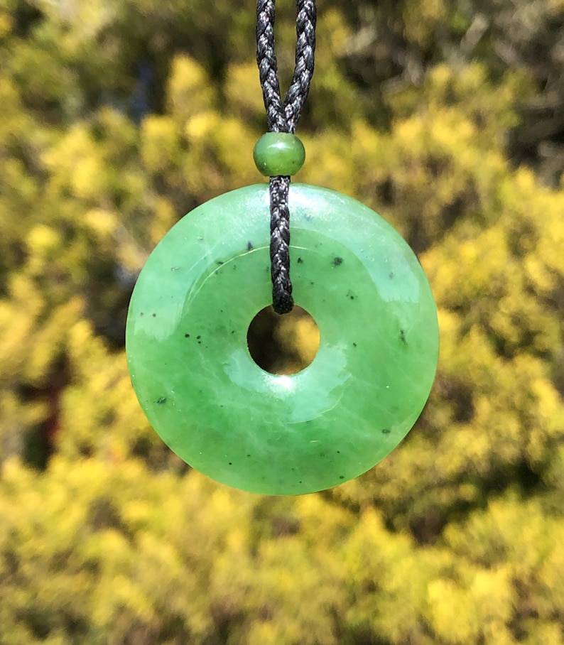 May include: A green jade pendant in the shape of a donut, hanging from a black cord.
