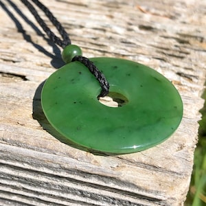 May include: A green jade pendant in the shape of a donut, hanging from a black cord.