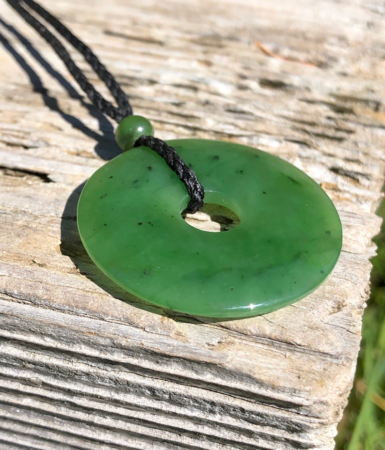 May include: A green jade pendant in the shape of a donut, hanging from a black cord.