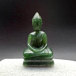May include: A small green jade Buddha statue sitting in a meditative pose. The statue is carved with intricate details and has a serene expression.
