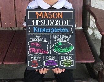 May include: A black chalkboard sign with the text "MASON First Day Of Kindergarten" in colorful letters. The sign also includes information about the child's teacher, age, date, and hobbies.