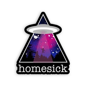 May include: A black triangle sticker with a white UFO and a pink and blue galaxy background. The text "homesick" is printed in white at the bottom of the sticker.