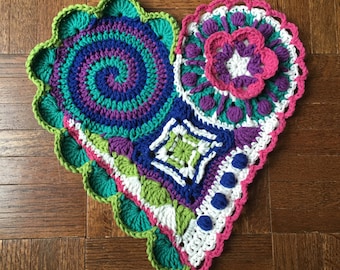 May include: A crocheted heart-shaped wall hanging with a variety of colorful patterns, including a spiral, a flower, and a geometric design.