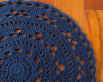 May include: A navy blue crocheted round rug with a circular pattern. The rug is made of yarn and has a delicate, lacy design.
